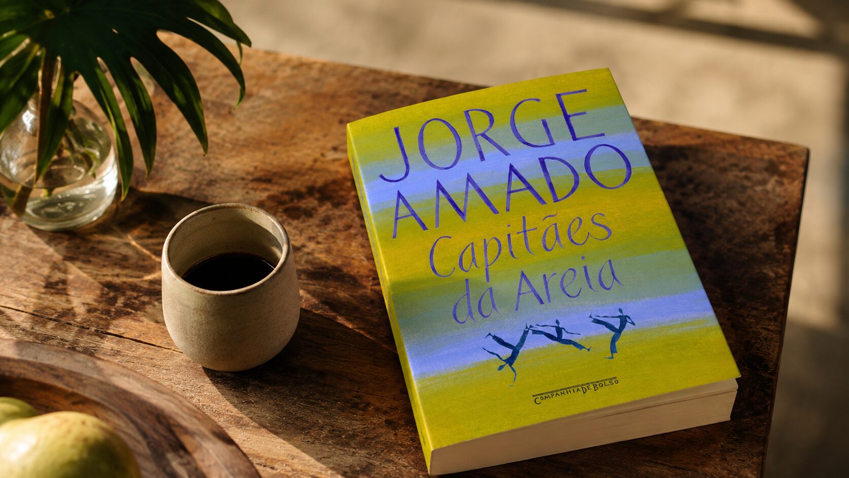 Livro Capitães da Areia, de Jorge Amado, sobre uma mesa de madeira ao lado de uma xícara de café