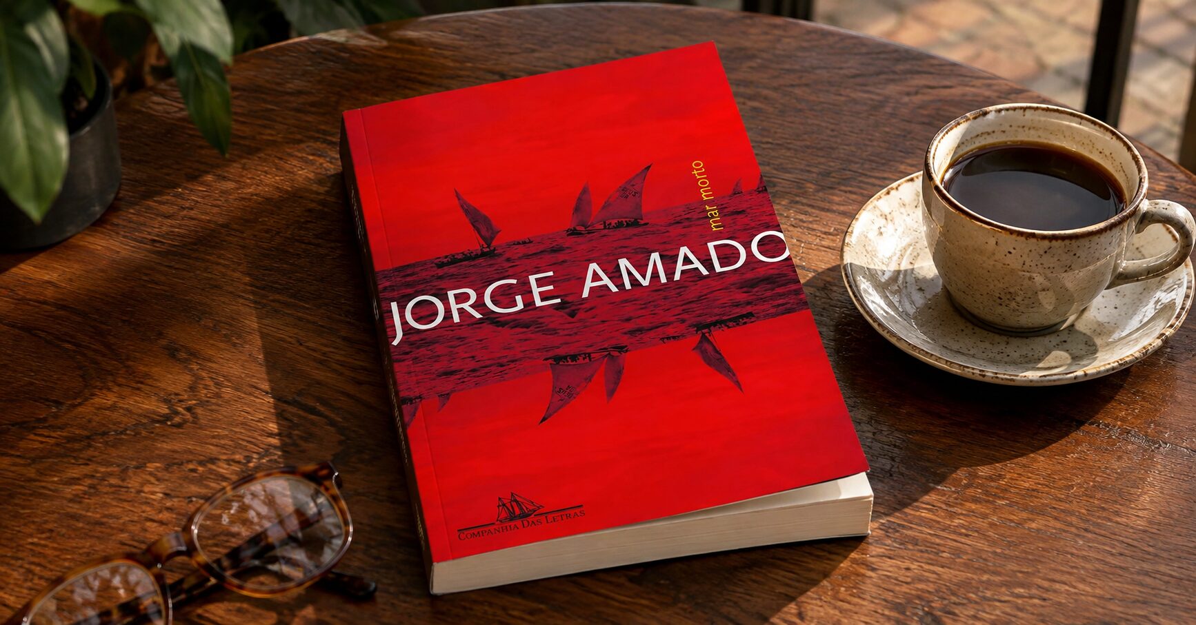 Livro Mar Morto, de Jorge Amado, sobre uma mesa de madeira ao lado de uma xícara de café e óculos