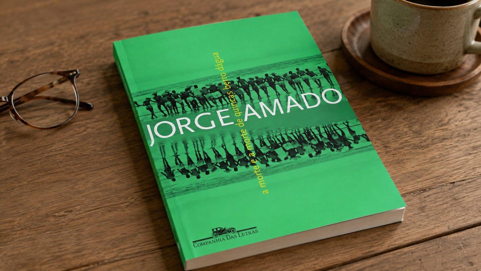 Edição especial de A morte e a morte de Quincas Berro D’Água, de Jorge Amado, sobre uma mesa de madeira com xícara e óculos.